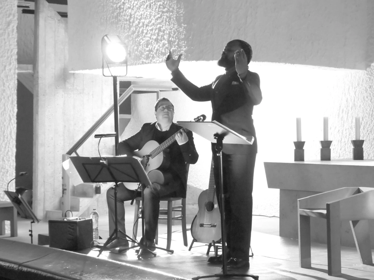 Serge Kakudji chante pendant que David Demange joue de la guitare à la chapelle de Ronchamp